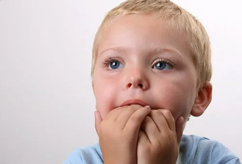 Un niño se mueve inquieto con las manos en la boca.