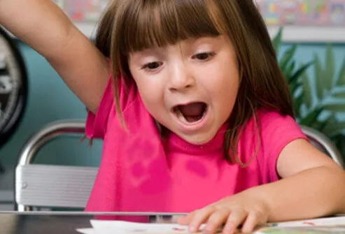 Una niña levanta la mano y grita una respuesta en clase.