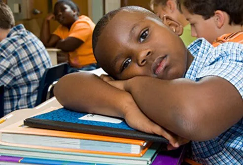 Un niño está soñando despierto en clase mientras otros estudiantes trabajan.